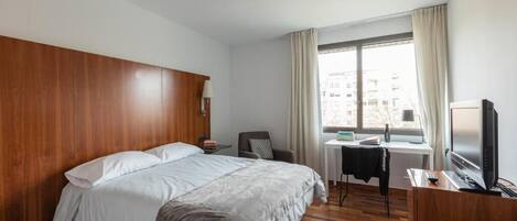 A hotel room with a large bed, a desk with a chair, a television, and a window with curtains.