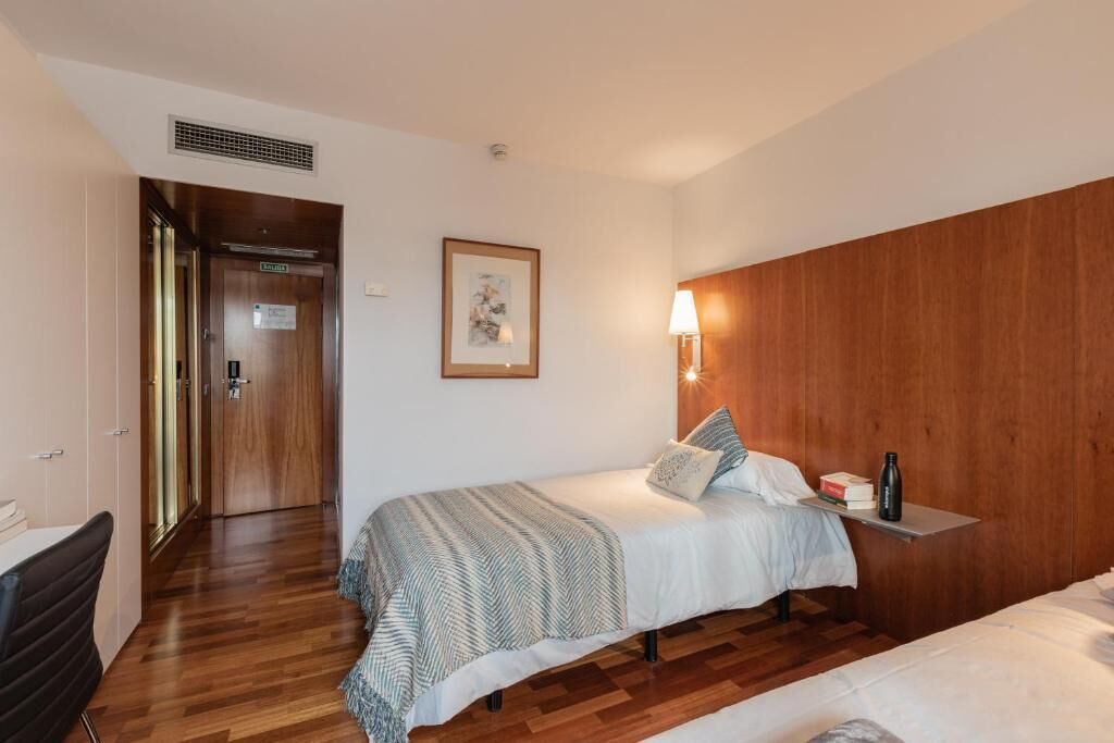 Een hotelkamer met een bed, nachtkastje, lamp en een lijst aan de muur.
