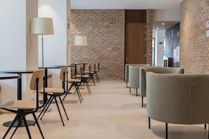 A modern hotel lobby with a brick wall, a reception desk, and a row of chairs and tables. - Micampus Pamplona  (Pamplona)