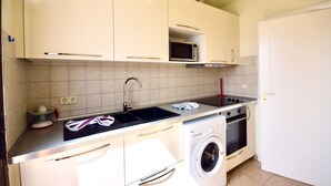 Een kleine keuken met witte kastjes, een ingebouwde magnetron, een spoelbak, een fornuis en een wasmachine.