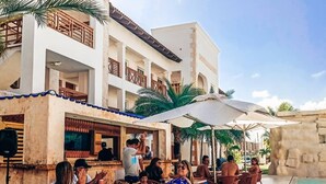 Uma área de refeições ao ar livre com mesas e cadeiras, piscina e um edifício com varandas.