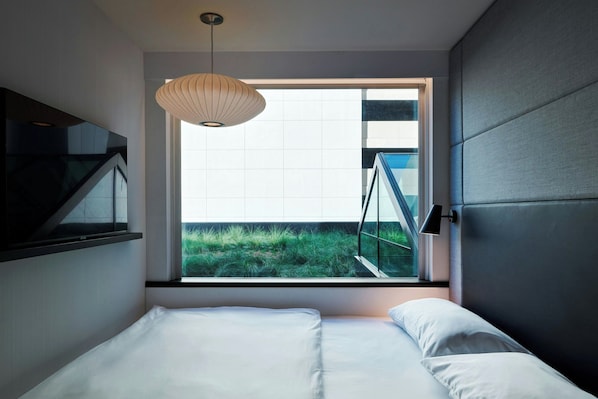 Un dormitorio moderno con un ventanal grande, una cama, una lámpara colgante y vistas a zonas verdes.