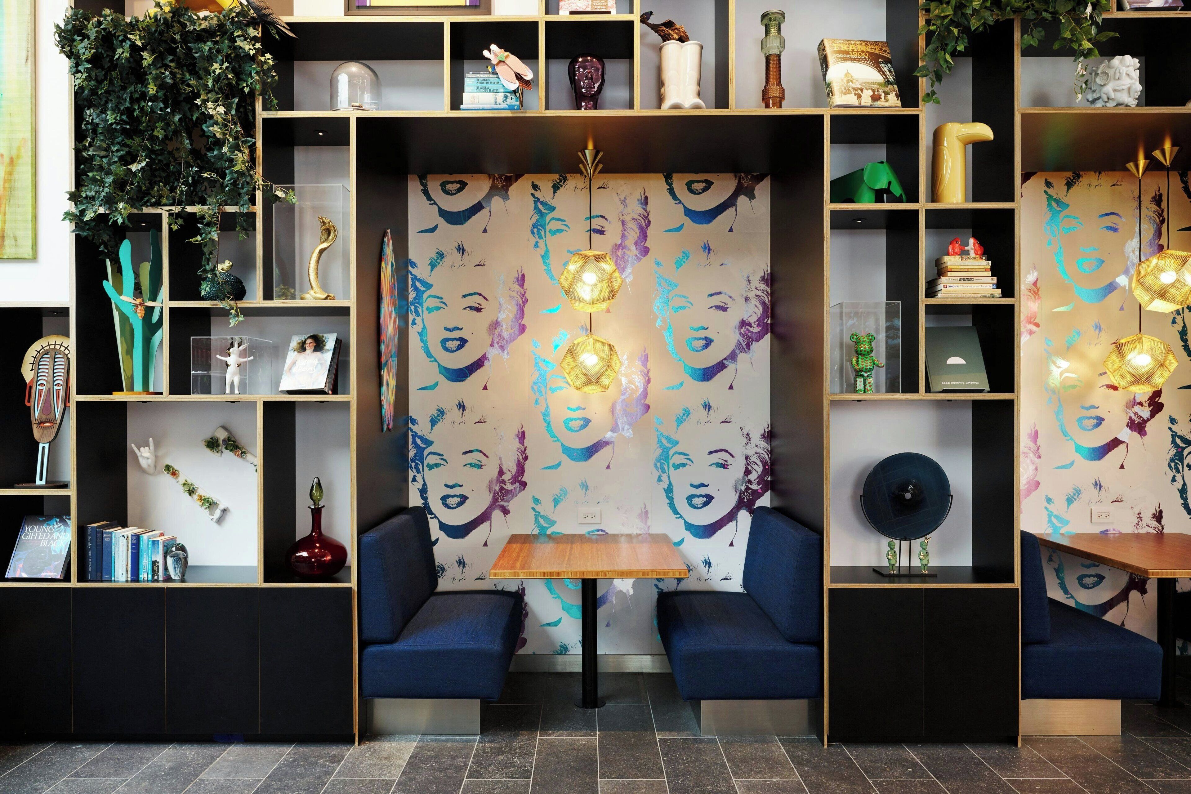 Un interior moderno con una zona de estar central, estanterías con diversos objetos decorativos y una pared con un diseño de rostros.