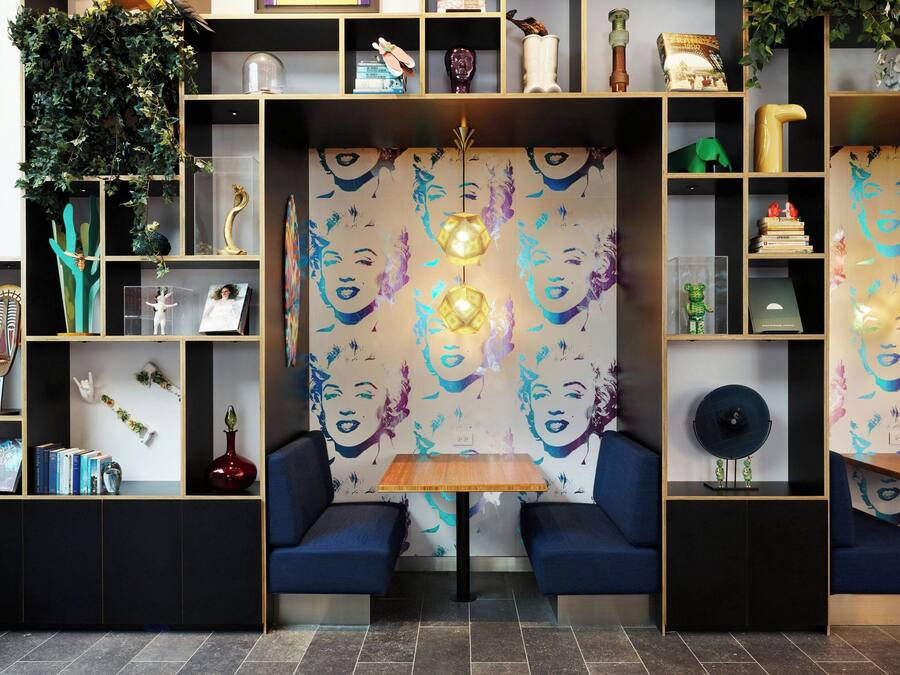 Un interior moderno con una zona de estar central, estanterías con diversos objetos decorativos y una pared con un diseño de rostros.