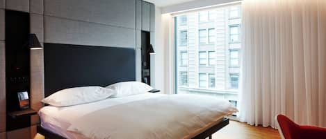 Un dormitorio moderno con una cama grande, un armario empotrado, una mesita de noche y vistas a un paisaje urbano a través de un amplio ventanal.