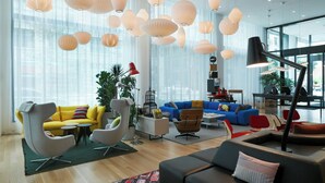 A modern living room with a yellow sofa, a blue sofa, and a black sofa. There are multiple hanging lights and a large window in the background.