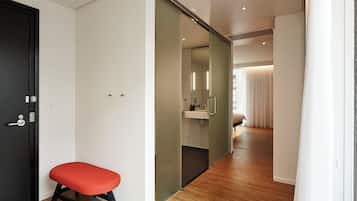 Een moderne hotelkamer met een houten vloer, een rode bank, een schuifdeur naar een badkamer en een bed met witte gordijnen.