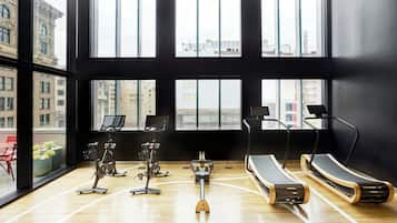 Un gimnasio moderno con equipamiento de ejercicio, amplias ventanas y vista al paisaje urbano.