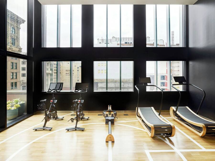 Un gimnasio moderno con equipamiento de ejercicio, amplias ventanas y vista al paisaje urbano.