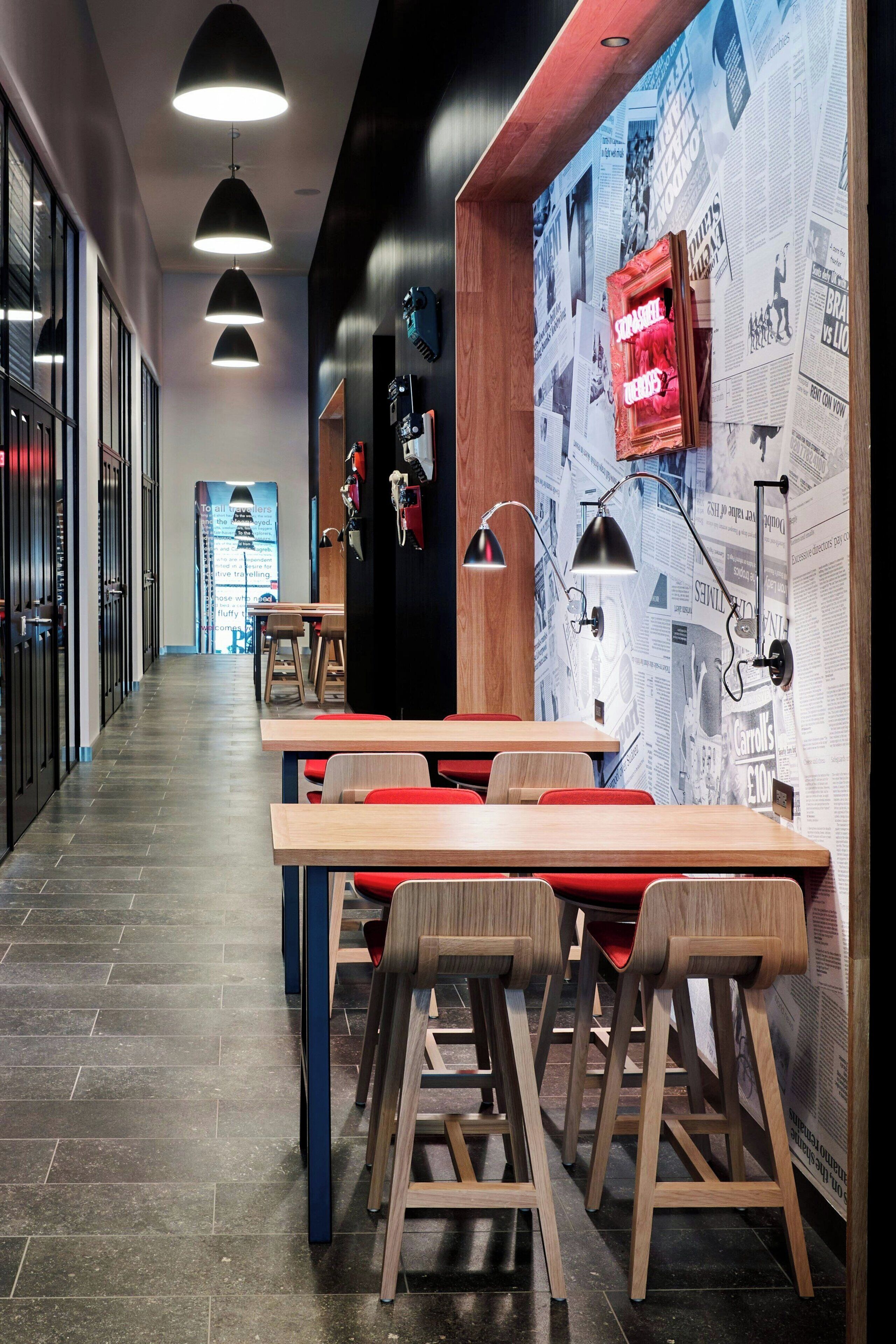 A modern interior with a long corridor, wooden tables, and chairs, and a wall with newspaper clippings.