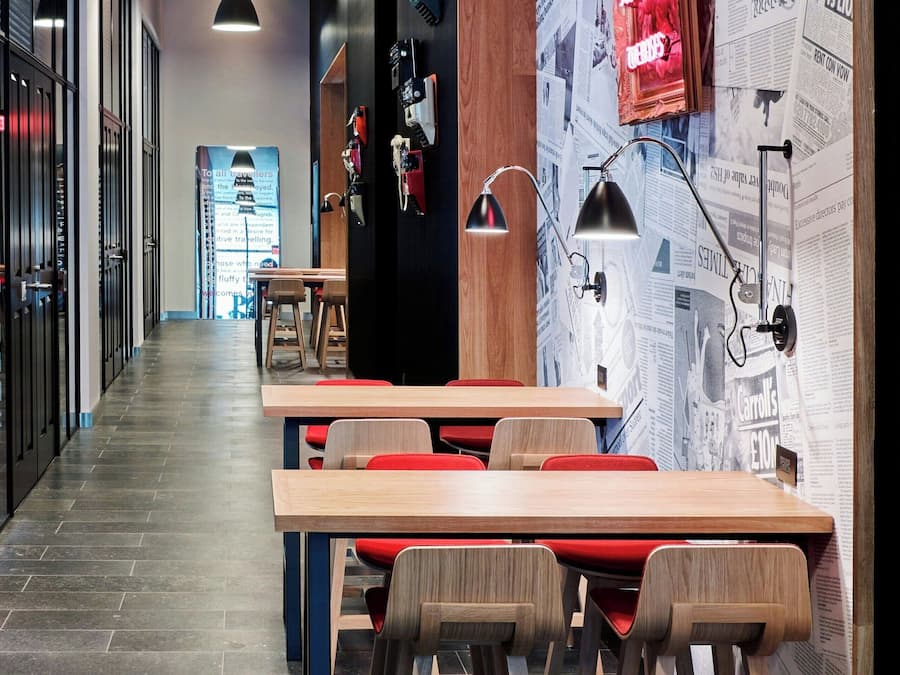 A modern interior with a long corridor, wooden tables, and chairs, and a wall with newspaper clippings.