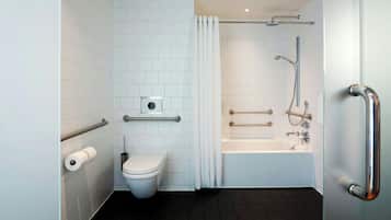 A modern bathroom with white tiles, a toilet, a bathtub with grab bars, and a shower area.