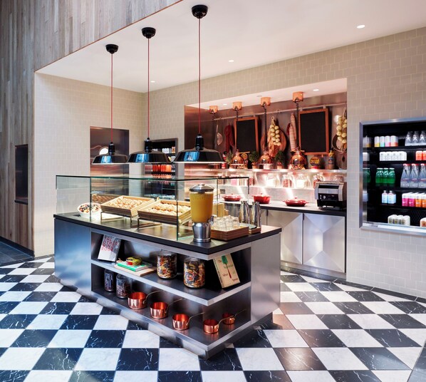 Una cafetería moderna con piso a cuadros, una vitrina con pasteles y diversas bebidas.