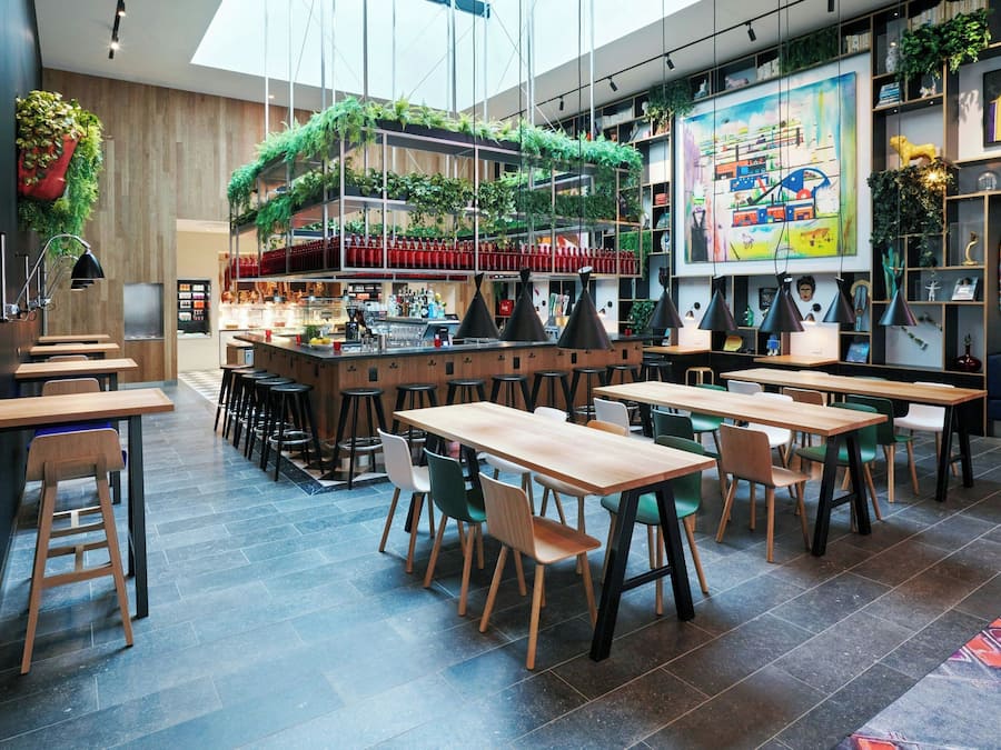 A modern cafe with wooden tables and chairs, a bar area, and green plants hanging from the ceiling.
