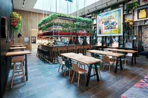 Un café moderne avec des tables et des chaises en bois, un coin bar et des plantes vertes suspendues au plafond.