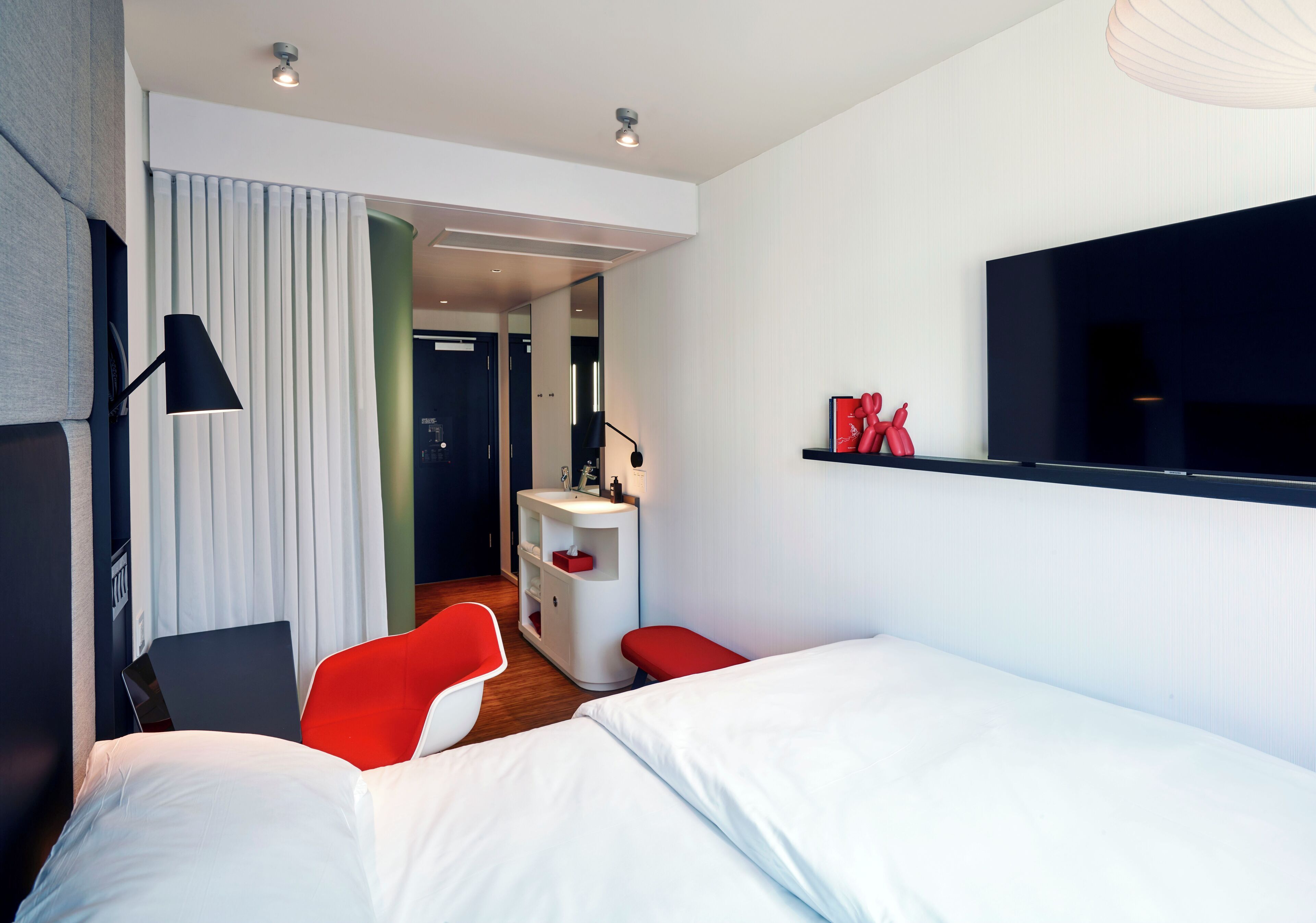 Une chambre d’hôtel moderne équipée d’un lit, d’un bureau, d’une chaise, d’une table de chevet, d’une télévision et d’une fenêtre avec des rideaux.