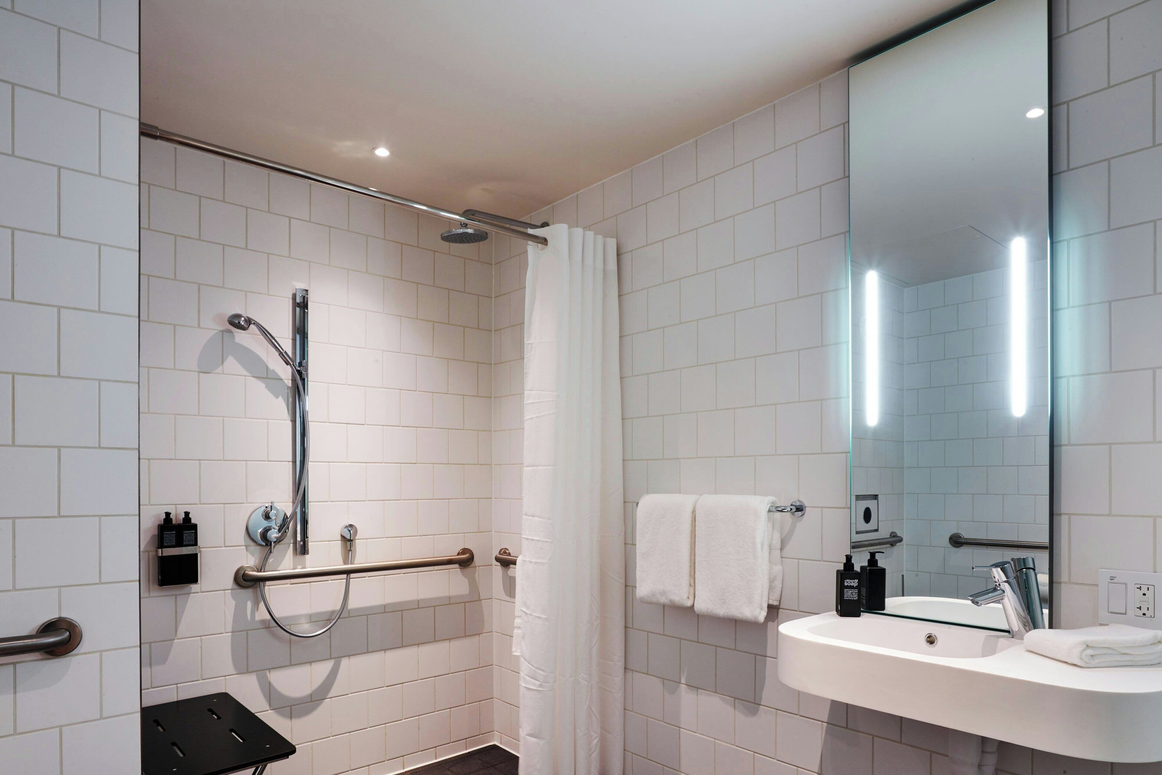 A modern bathroom with white tiled walls, a glass shower enclosure, a white sink with a mirror, and a towel rack.