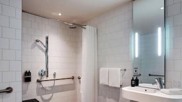 A modern bathroom with white tiled walls, a glass shower enclosure, a white sink with a mirror, and a towel rack.