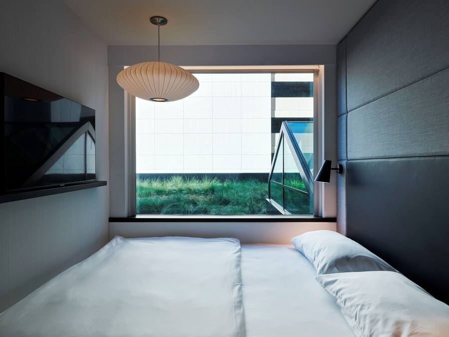 A modern bedroom with a large window, a bed, and a hanging light fixture.