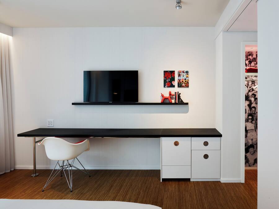 Una habitación moderna con un escritorio negro, una silla blanca y un televisor montado.