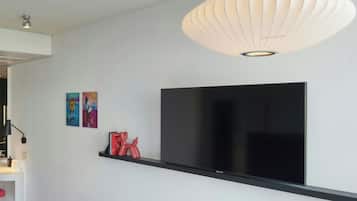 Un saló modern amb un gran televisor de pantalla plana fixat a una estant negra, una paret blanca i una làmpada penjant única en forma de farol de paper.