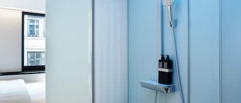 A modern bathroom with a glass shower enclosure, a handheld showerhead, and a wall-mounted control panel.