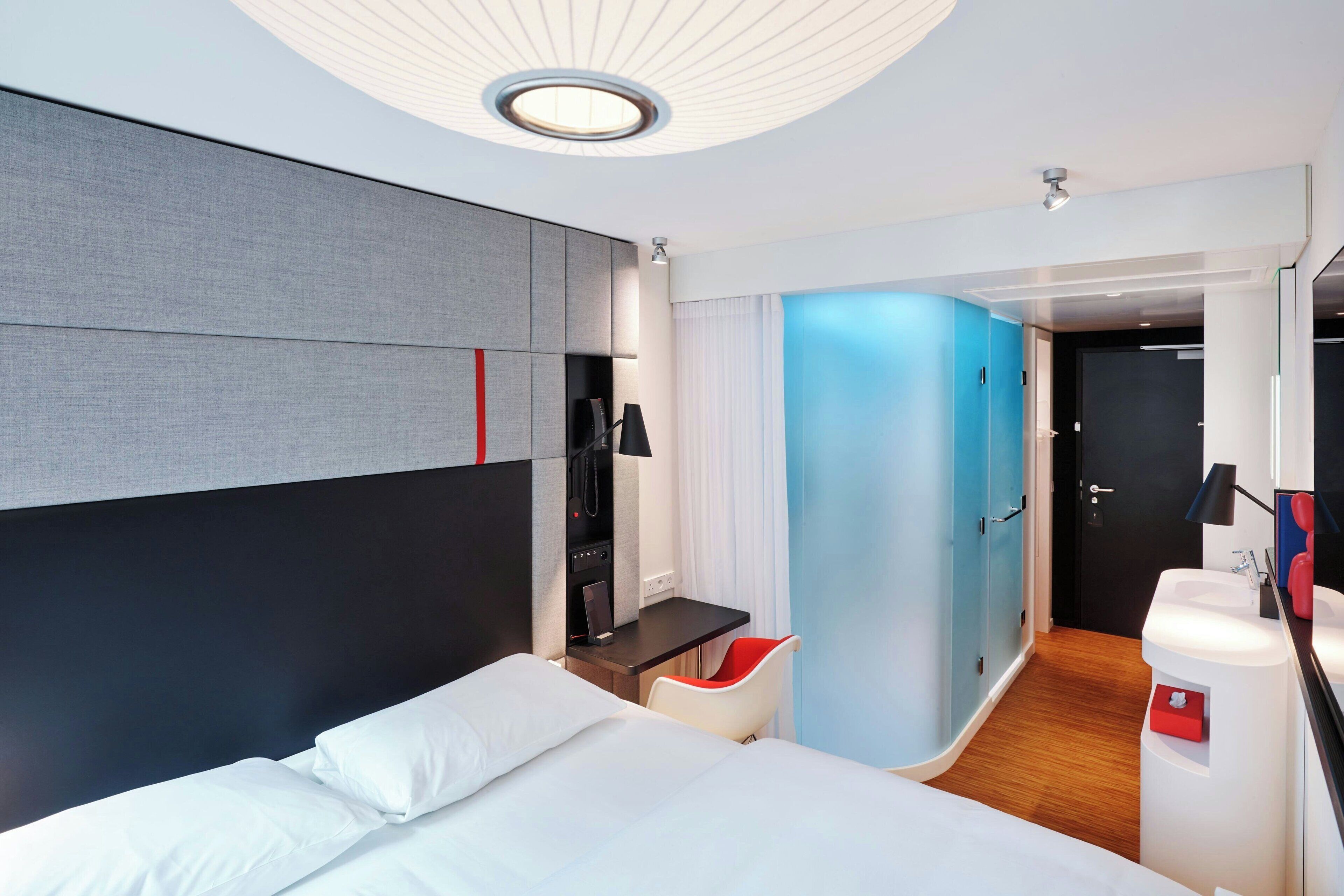 Une chambre d’hôtel moderne dotée d’un grand lit, d’un bureau, d’une chaise, d’une salle de bain et d’une porte donnant sur une autre pièce.