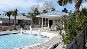 Uma área de piscina com vários jatos de água, um espaço coberto para sentar e um edifício com telhado de metal.