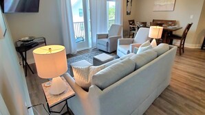 Sala de estar com sofá, cadeiras, televisão e área de jantar com mesa e cadeiras.