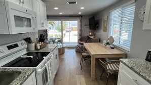 Una cocina moderna con armarios blancos, horno empotrado y comedor con mesa y sillas de madera.