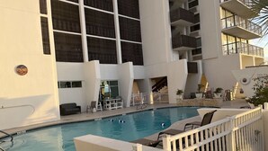 A swimming pool with lounge chairs and a white fence. - Condo right on the beach! Stunning seventh floor views! (Galveston)