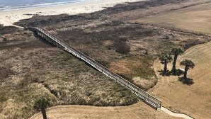 An aerial view of a beach with a long wooden boardwalk leading to the shore. - Condo right on the beach! Stunning seventh floor views! (Galveston)