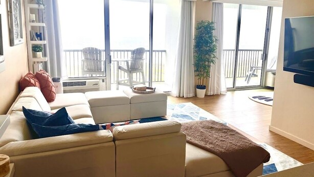 A living room with a sofa, a TV, and a balcony with chairs. - Condo right on the beach! Stunning seventh floor views! (Galveston)