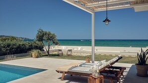 Zona junto a la piscina con sillones de descanso, una mesa de madera y vistas al océano.