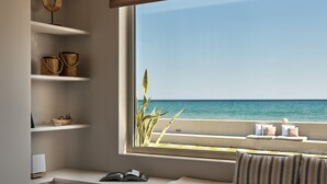 Una habitación con vista al mar, un asiento junto a la ventana con cojines, estantes con cestas y un ordenador portátil en el alféizar.