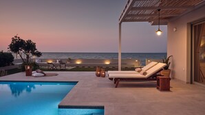Zona junto a la piscina con sillones de descanso y vista al océano al atardecer.