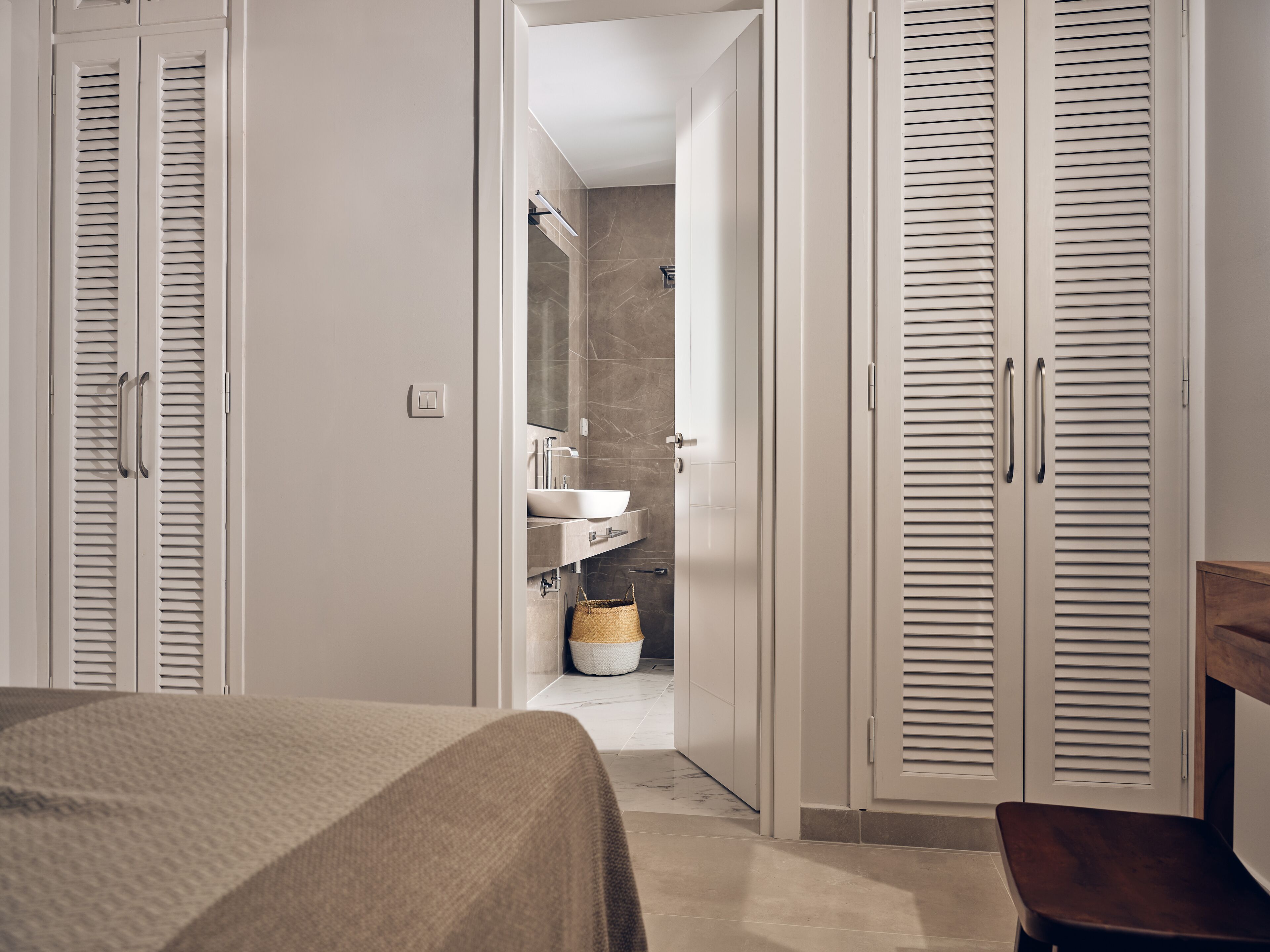 A bedroom with a bed, a wooden bench, and a bathroom with a sink and mirror.
