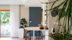Une cuisine moderne avec une table de salle à manger ronde, deux tabourets de bar, une machine à café et une plante.