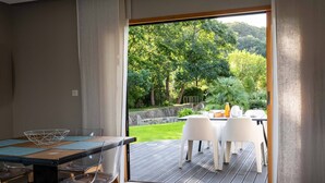 Un espace de restauration moderne avec une table et des chaises, donnant sur un jardin luxuriant grâce à une porte ouverte.