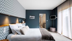 Une chambre d’hôtel moderne avec un grand lit, un téléviseur fixé au mur et une vue sur la salle de bain grâce à une porte ouverte.