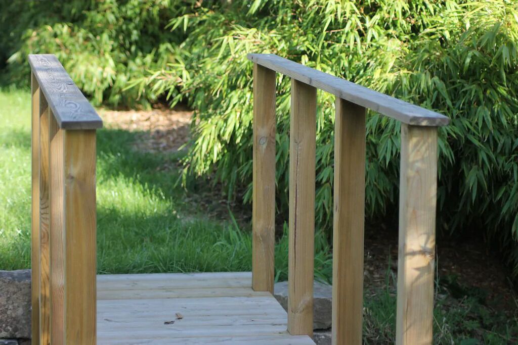 A wooden deck with a simple railing, surrounded by greenery.