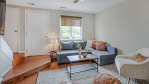 A living room with a sofa, coffee table, and armchair, a staircase, and a ceiling fan. - Postcards from the Bay (Norfolk)