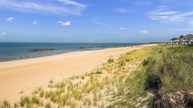 A beach with a clear sky, sandy shore, and grassy dunes. - Postcards from the Bay (Norfolk)