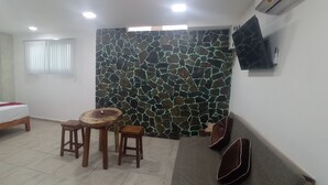 Un dormitorio con una cama, una mesa de madera, dos taburetes, un televisor y una pared de piedra.