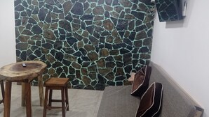 Una habitación con pared de piedra, una mesa de madera, dos taburetes, un sofá gris y una guitarra.
