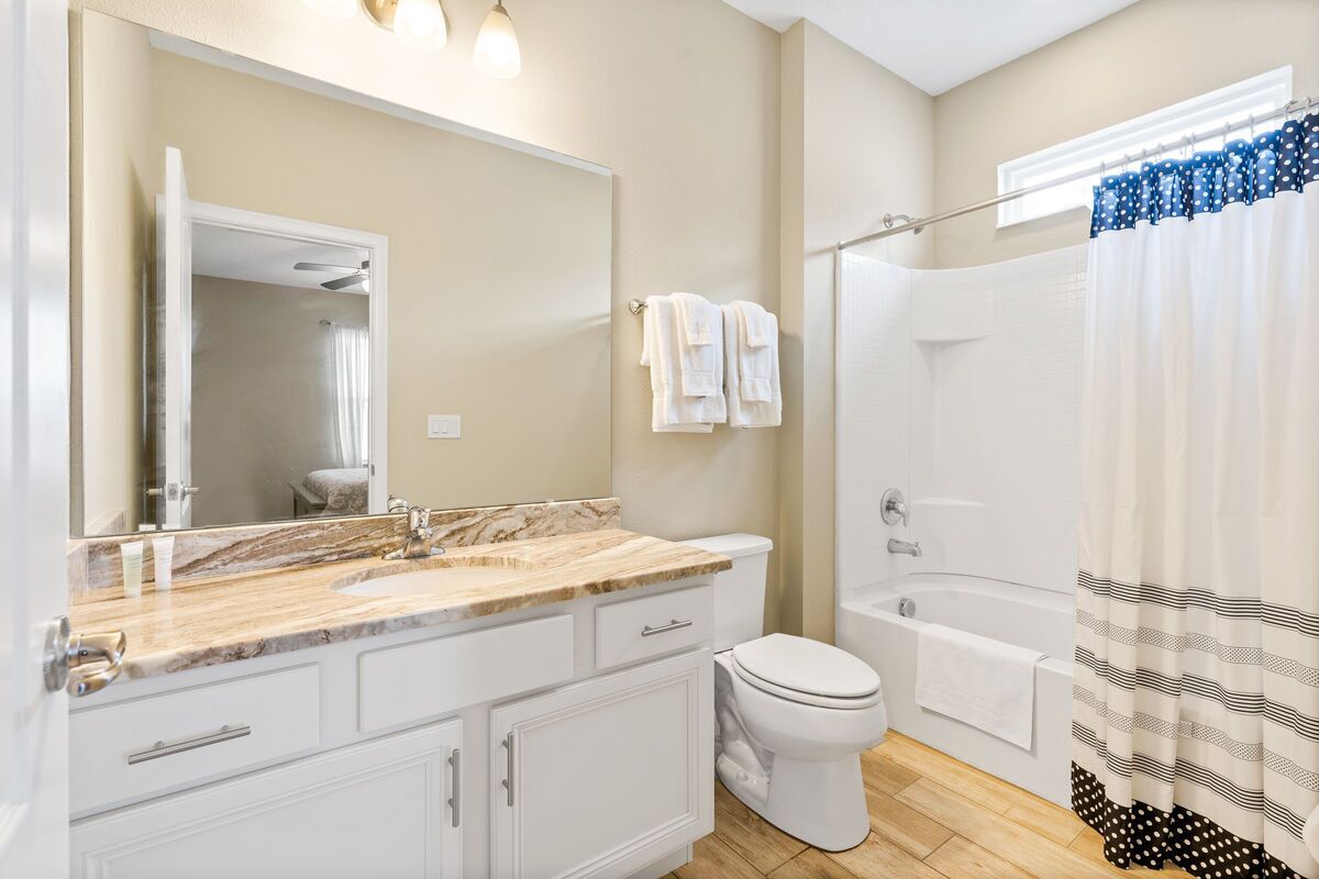 Une salle de bain avec un lavabo en marbre, des meubles blancs, des toilettes, une baignoire et un rideau de douche.
