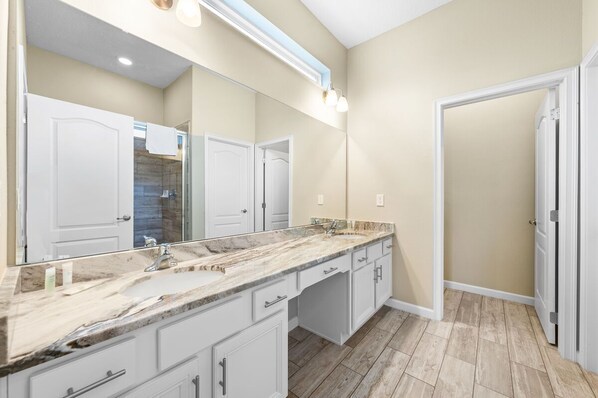 A bathroom with a large mirror, a marble countertop, and a shower area. - Home with Screened Pool Area | Pool Table and Video Games (Davenport)