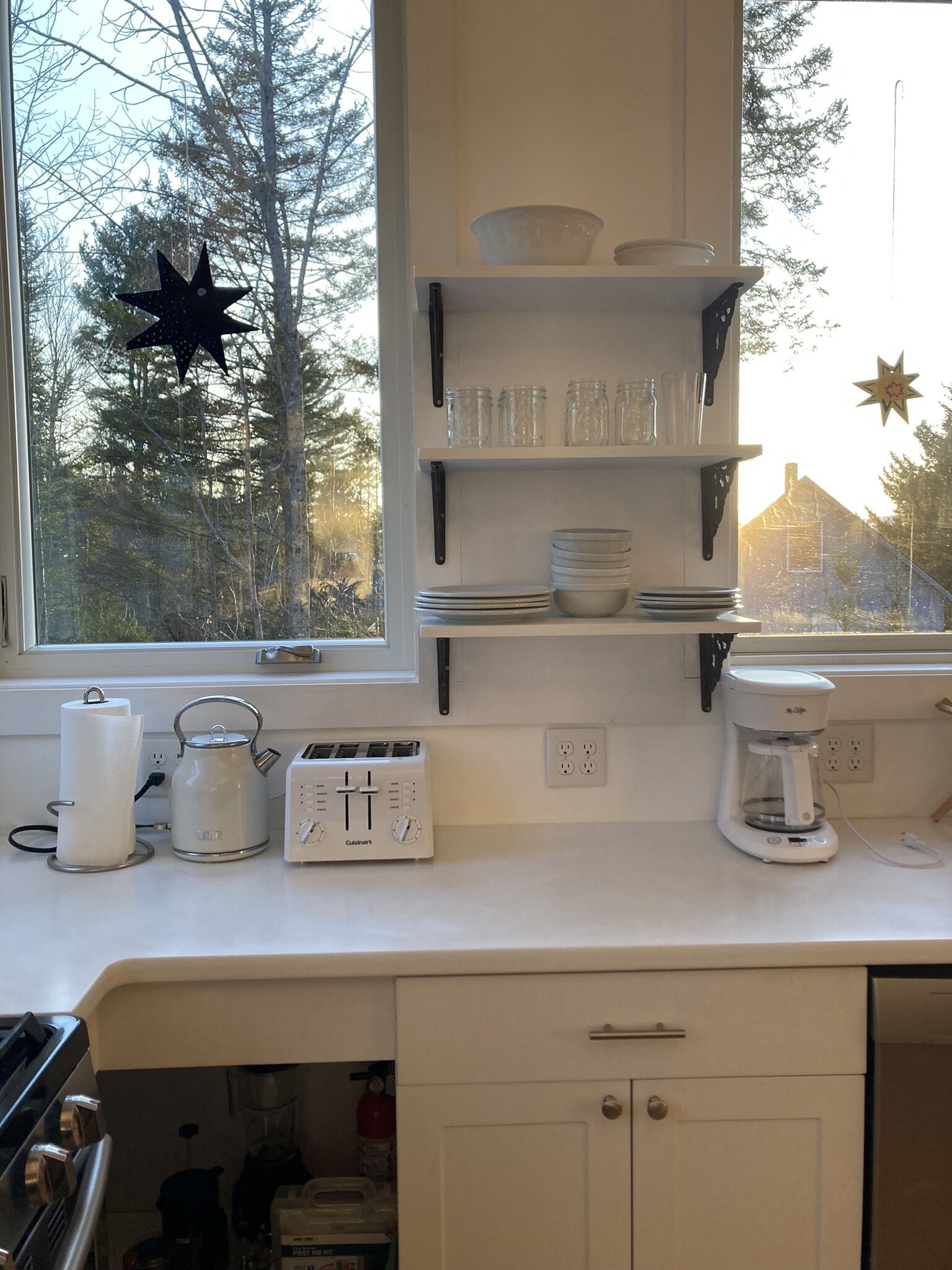 A kitchen with white cabinets, a window with a view of trees, and various kitchen appliances.