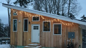 En stuga byggd av trä med en vit dörr, flera fönster och en liten veranda.