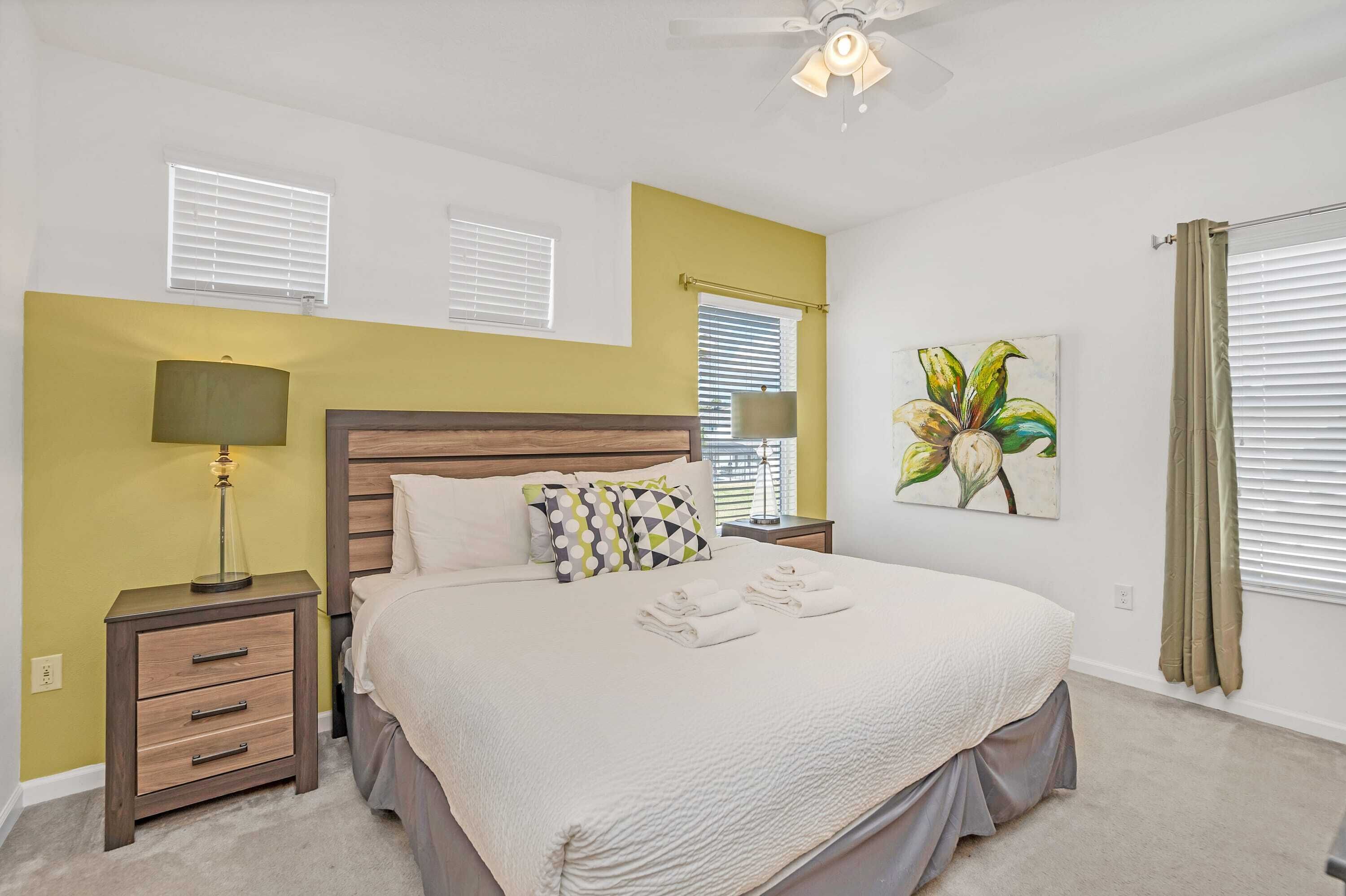 A bedroom with a bed, two bedside tables, a ceiling fan, and a window with blinds.